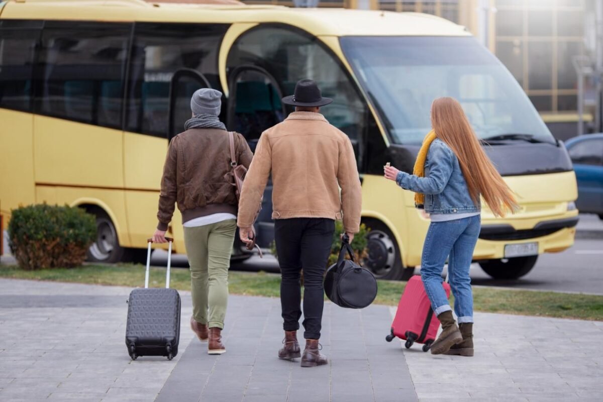 Three travelers with luggage walking towards a yellow shuttle bus at the airport.