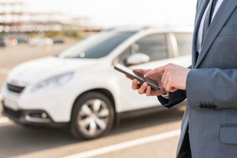 Businessman using a smartphone near a parked car in a parking lot.