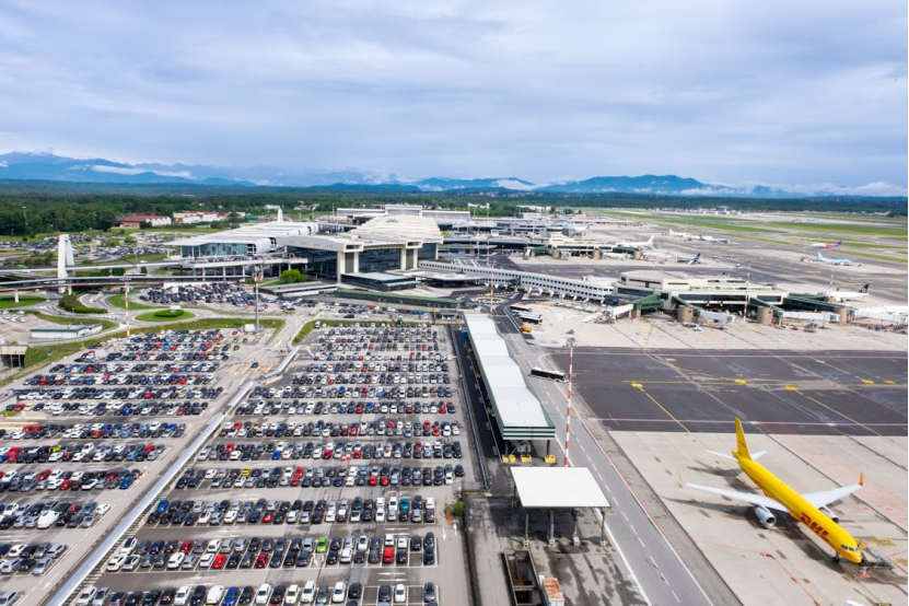 Aerial view of an airport with a large parking lot filled with cars and runways in the background.