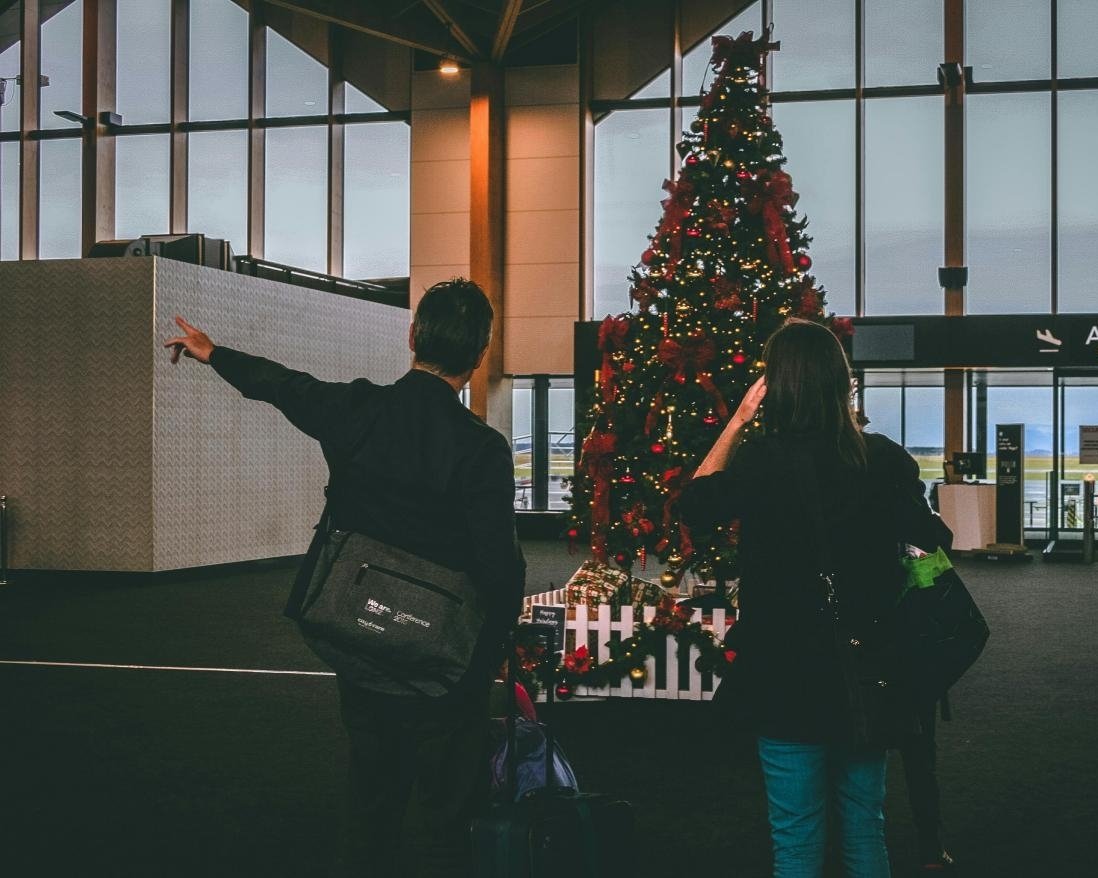 Couple at airport in front of a Christmas tree.